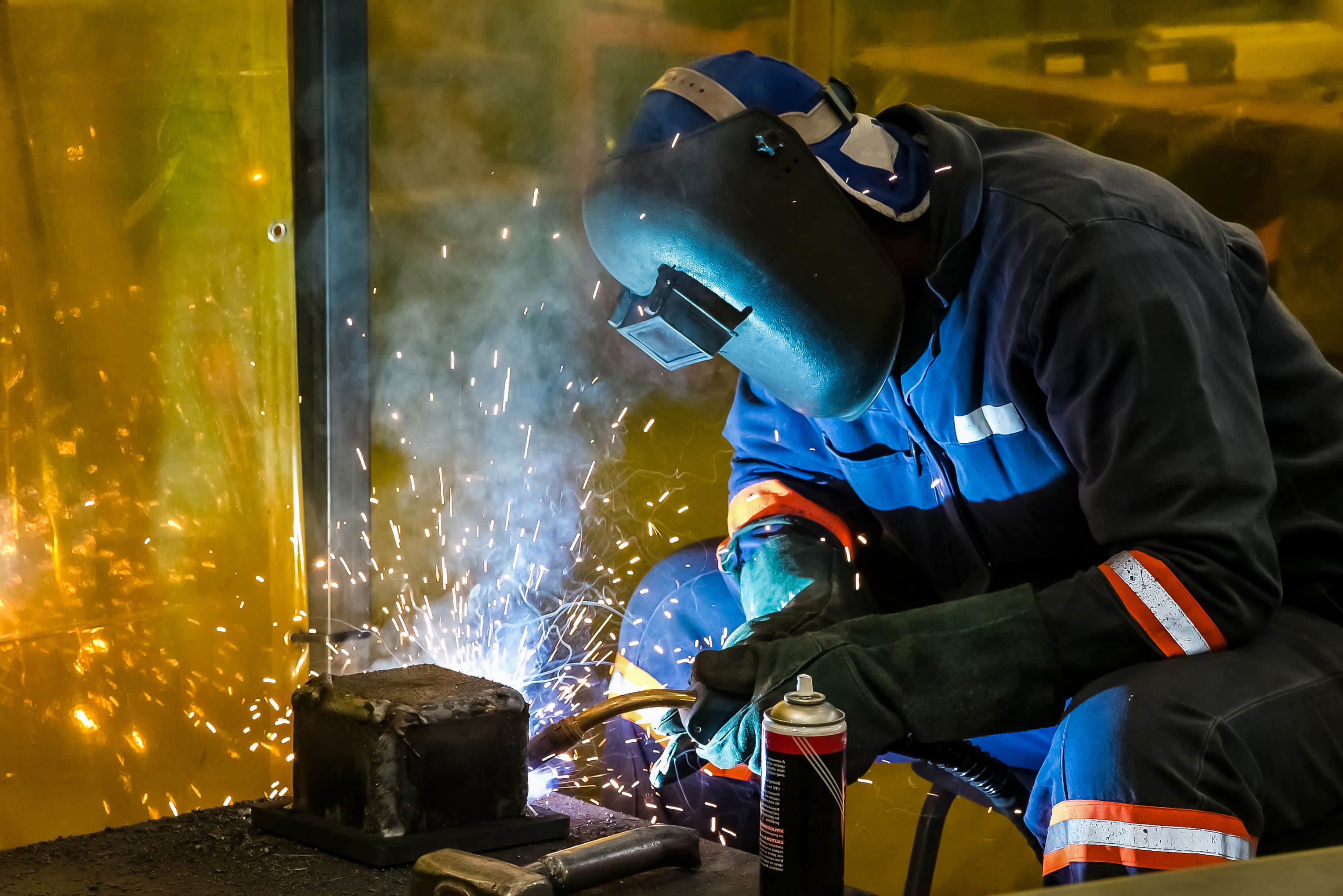 A certified welder performs manual welding on an industrial damper in the workshop.