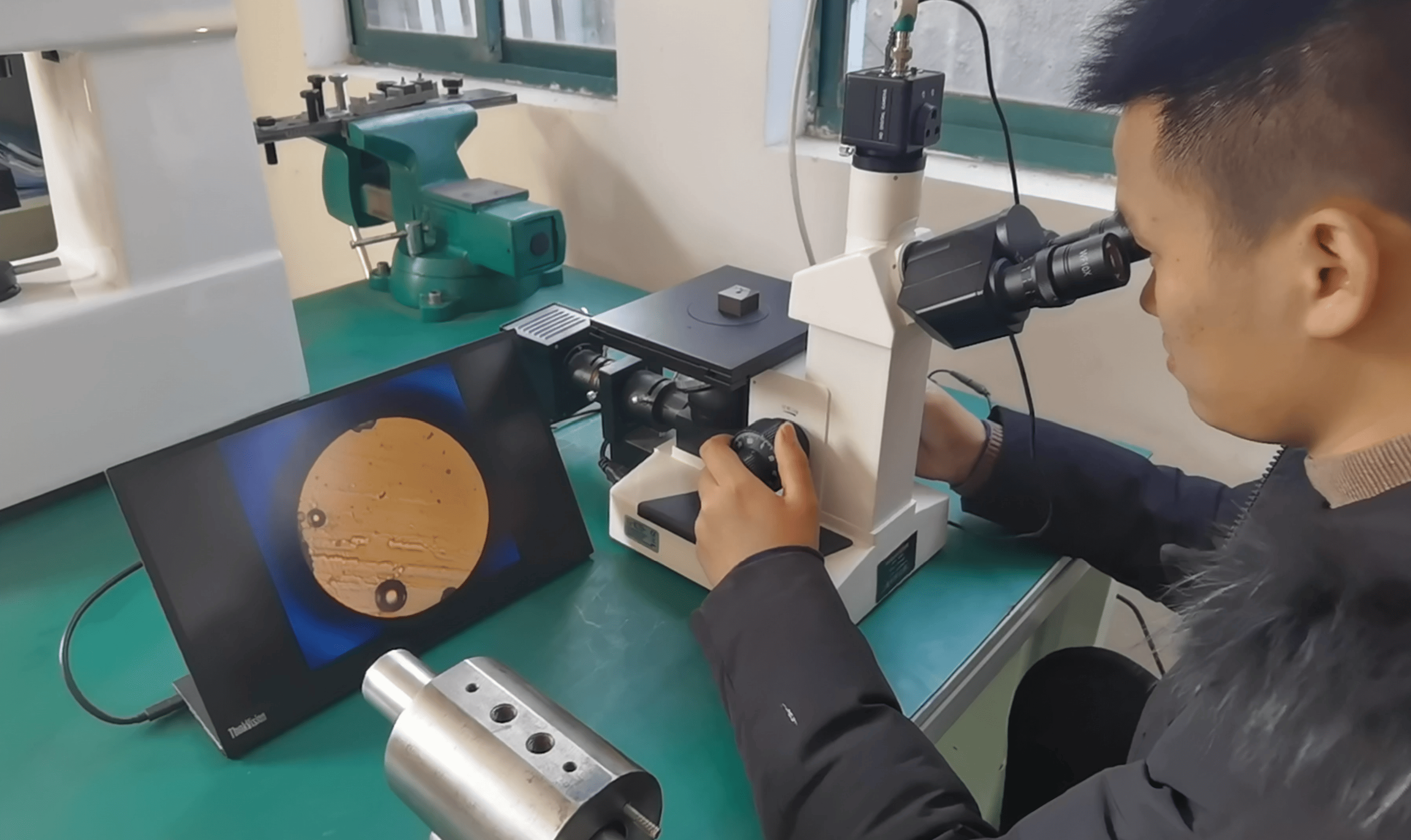 An inspector uses a metallurgical microscope to analyze metal parts for industrial dampers.